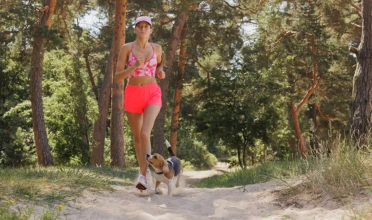 sporty woman and beagle dog runs in forest among trees. fitness, yoga for health of body and mental state
